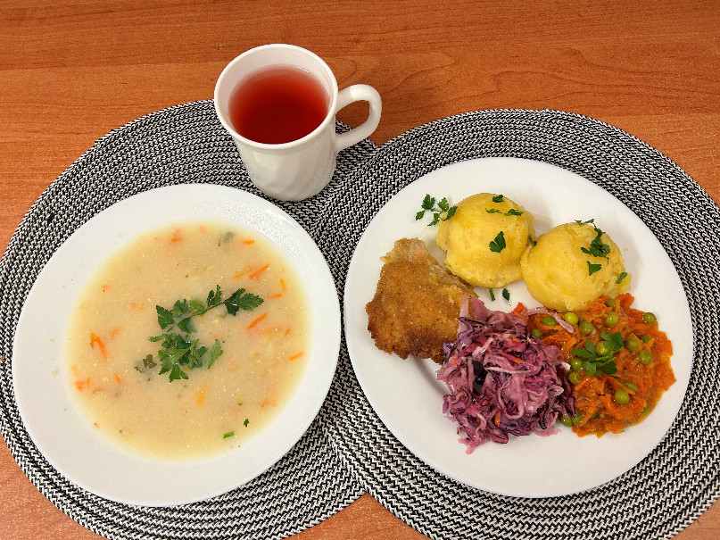 Na zdjęciu znajduje się: Jarzynowa z zacierką, Ziemniaki, Kotlet drobiowy panierowany, Sos pietruszkowy, Marchewka z groszkiem oprószana, Kompot owocowy, Surówka wykwintna z olejem